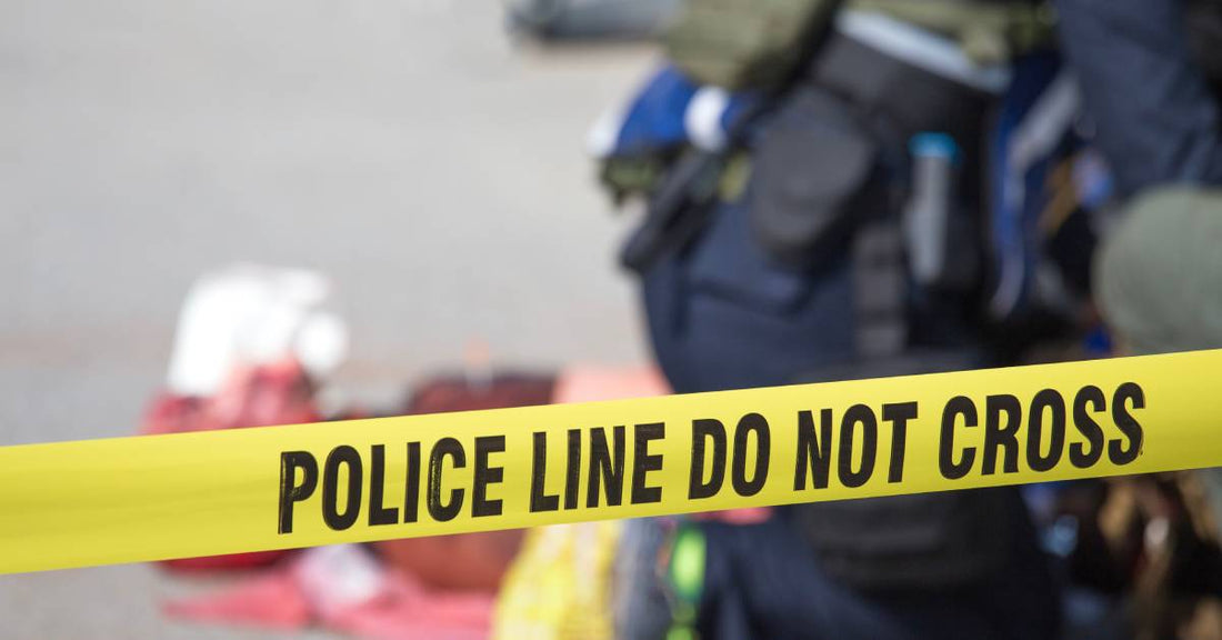Caution tape that says "police line do not cross." Blurred in the background is an officer applying first aid to a victim.
